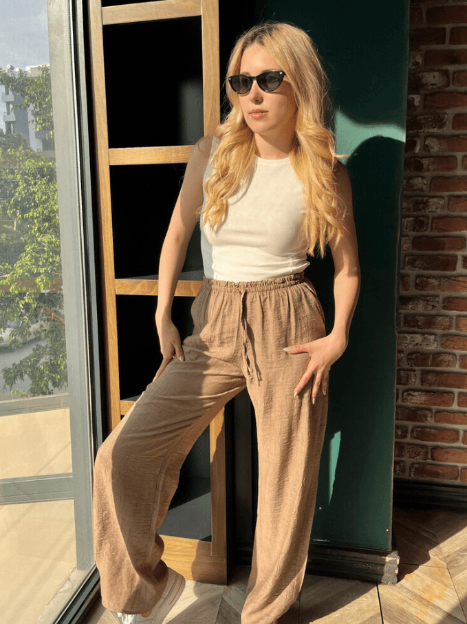 Beyaz Askılı tişört ve cep detaylı kahverengi keten pantolon giyen sarı saçlı kadın.