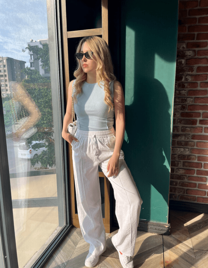 Beyaz Cepli Keten Pantolon ve mavi askılı giyen gözlüklü sarı saçlı kadın.