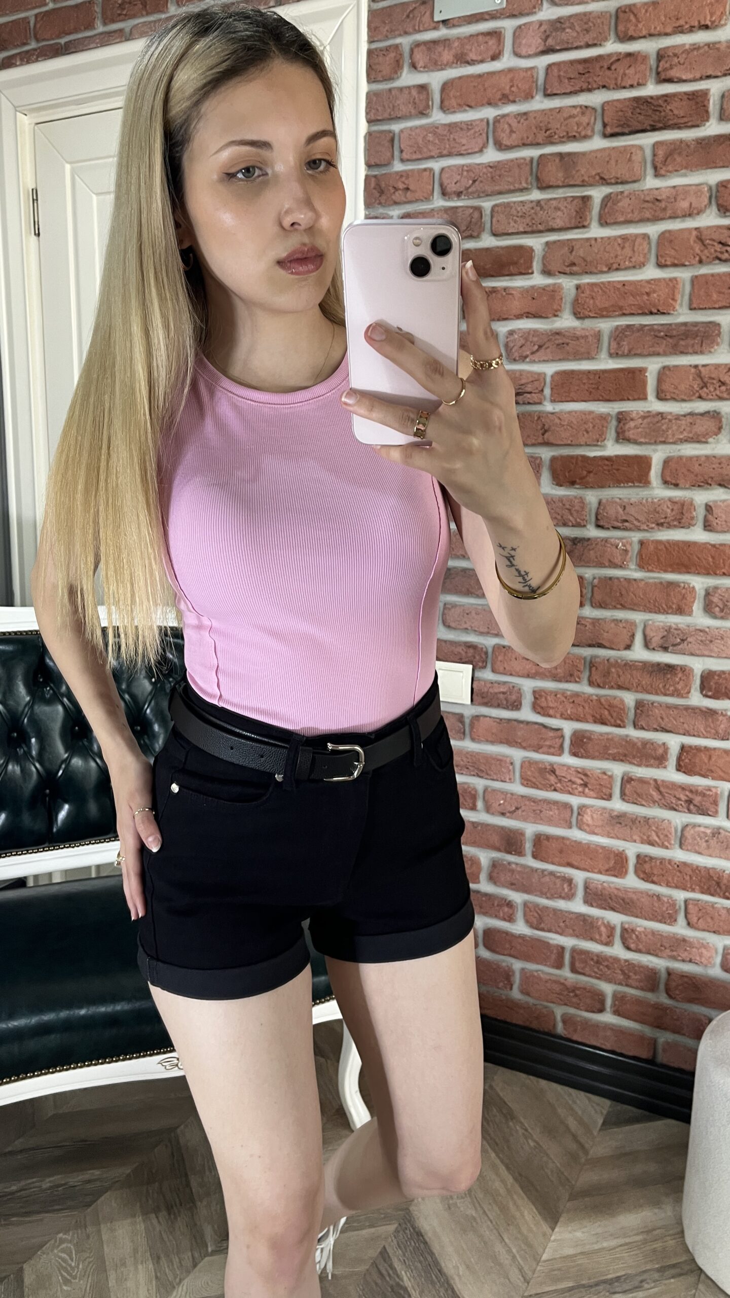 Kemerli siyah kot şort ve pembe bluz giyen sarı saçlı kadın.